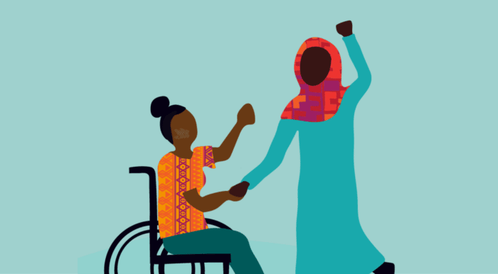 Illustation of a woman in a wheelchair is holding hands with another woman. Their other hands are raised in the air in fists.
